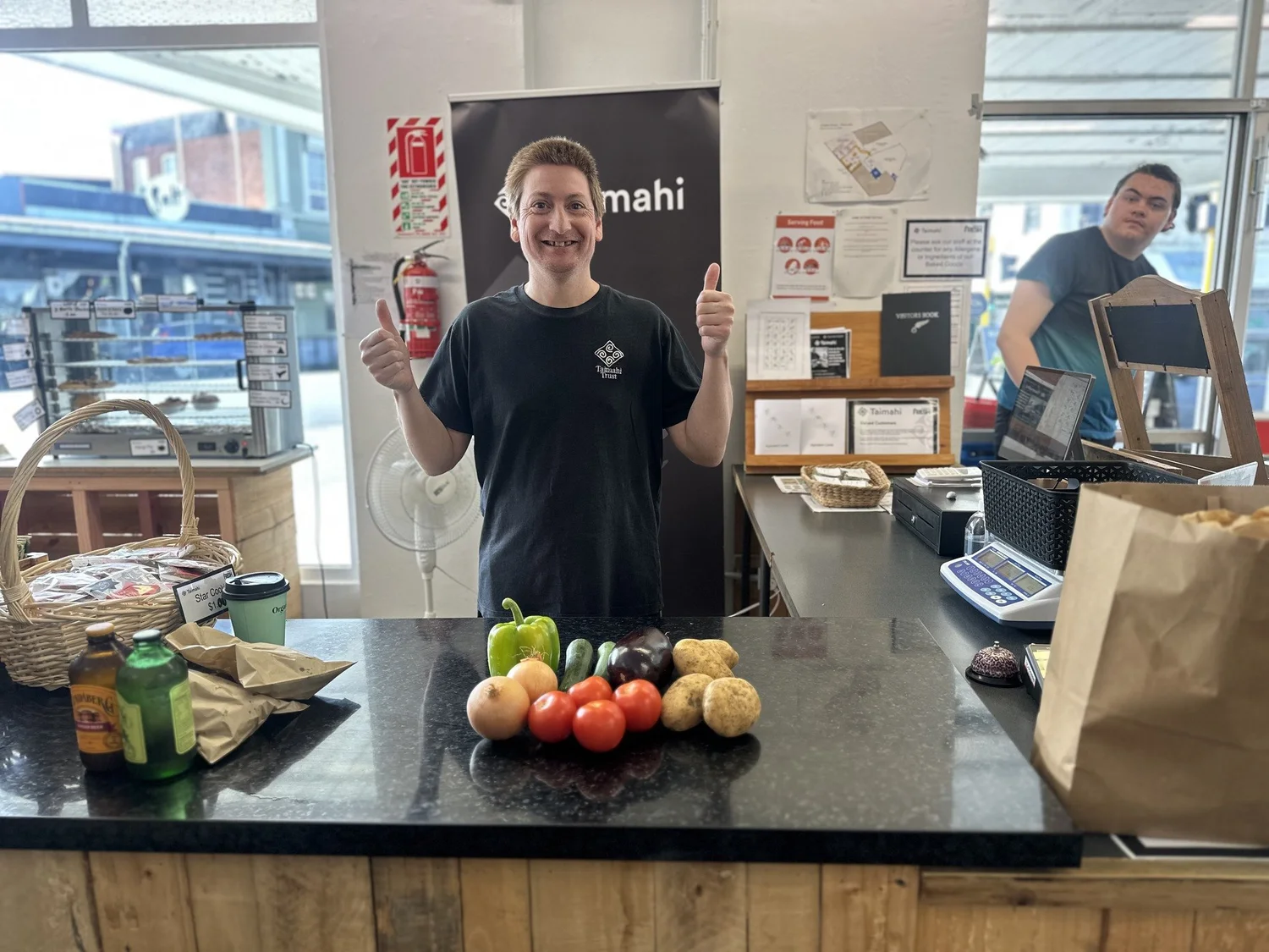 A Taimahi trainee standing behind the checkout with his thumbs up.